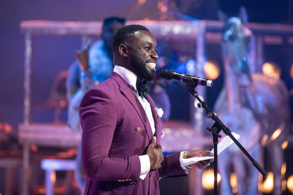 Emmanuel Ohene Boafo staat met een grote glimlach voor een microfoon, in een prachtig violet pak.